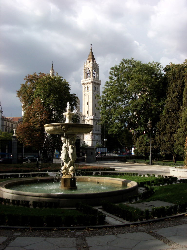 Fountain in foreground in Parque Del Retiro, Calle de Alcalá in the middle ground, and an unnamed church in the background. Near the Retiro metro stop.